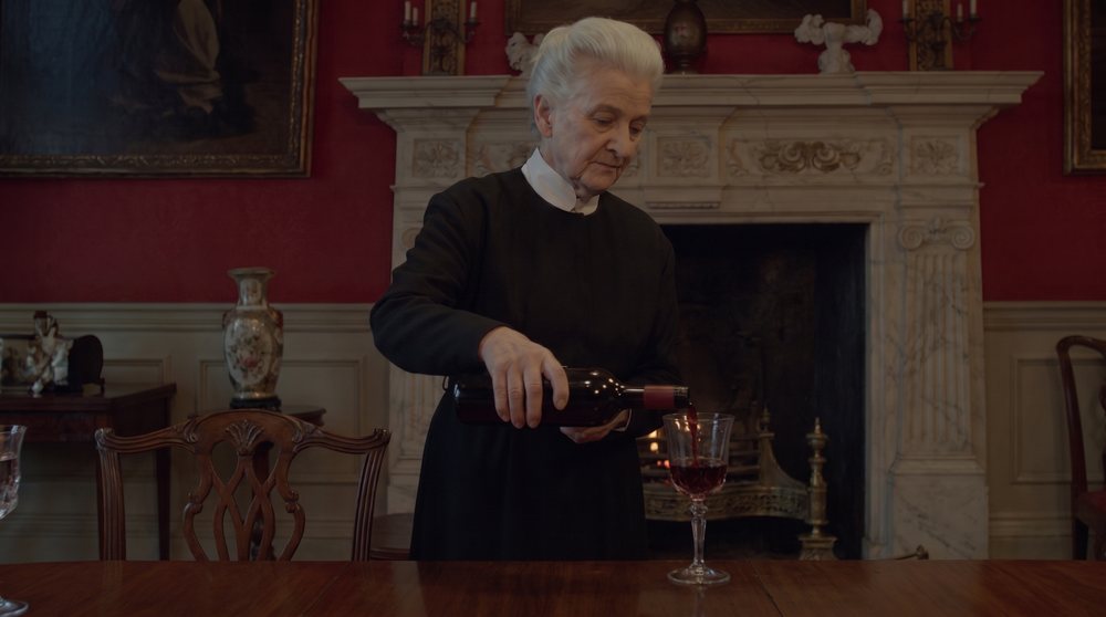 Reference: a housekeeper pours wine in a dark, moody red dining room